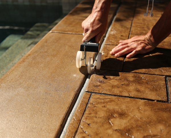 Technician setting closed cell backer rod to a uniform depth in a pool deck expansion joint with a roller tool